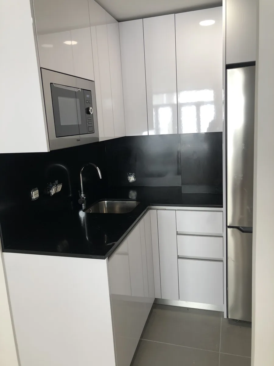 Cocina compacta reformada con mobiliario blanco y electrodomésticos integrados