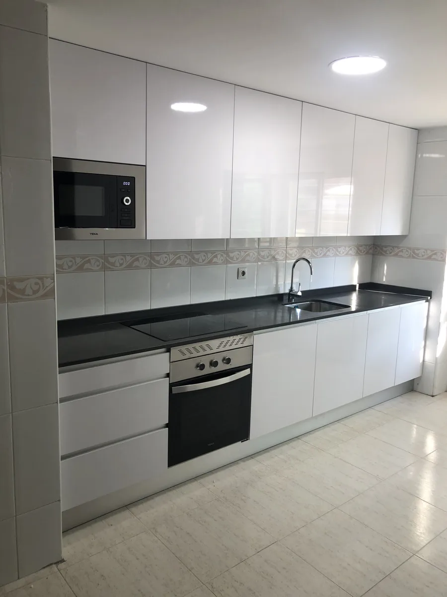 Cocina lineal terminada con muebles blancos, encimera negra y franja decorativa