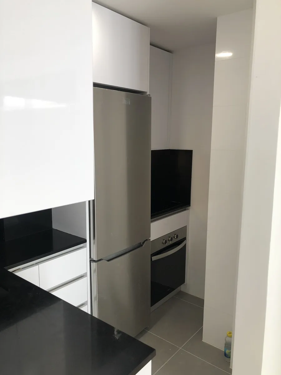 Zona de frigorífico y columna de horno en cocina blanca con encimera negra
