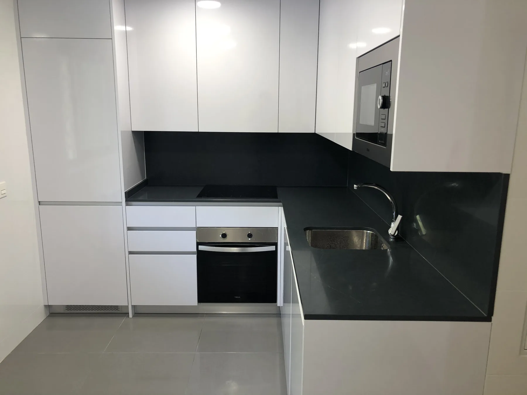 Cocina reformada con muebles blancos y encimera negra