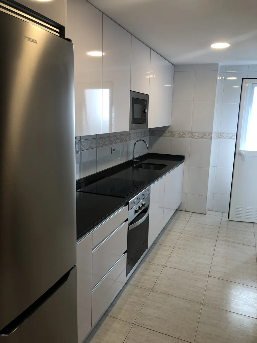 Cocina reformada vista desde el acceso con encimera negra y suelo claro