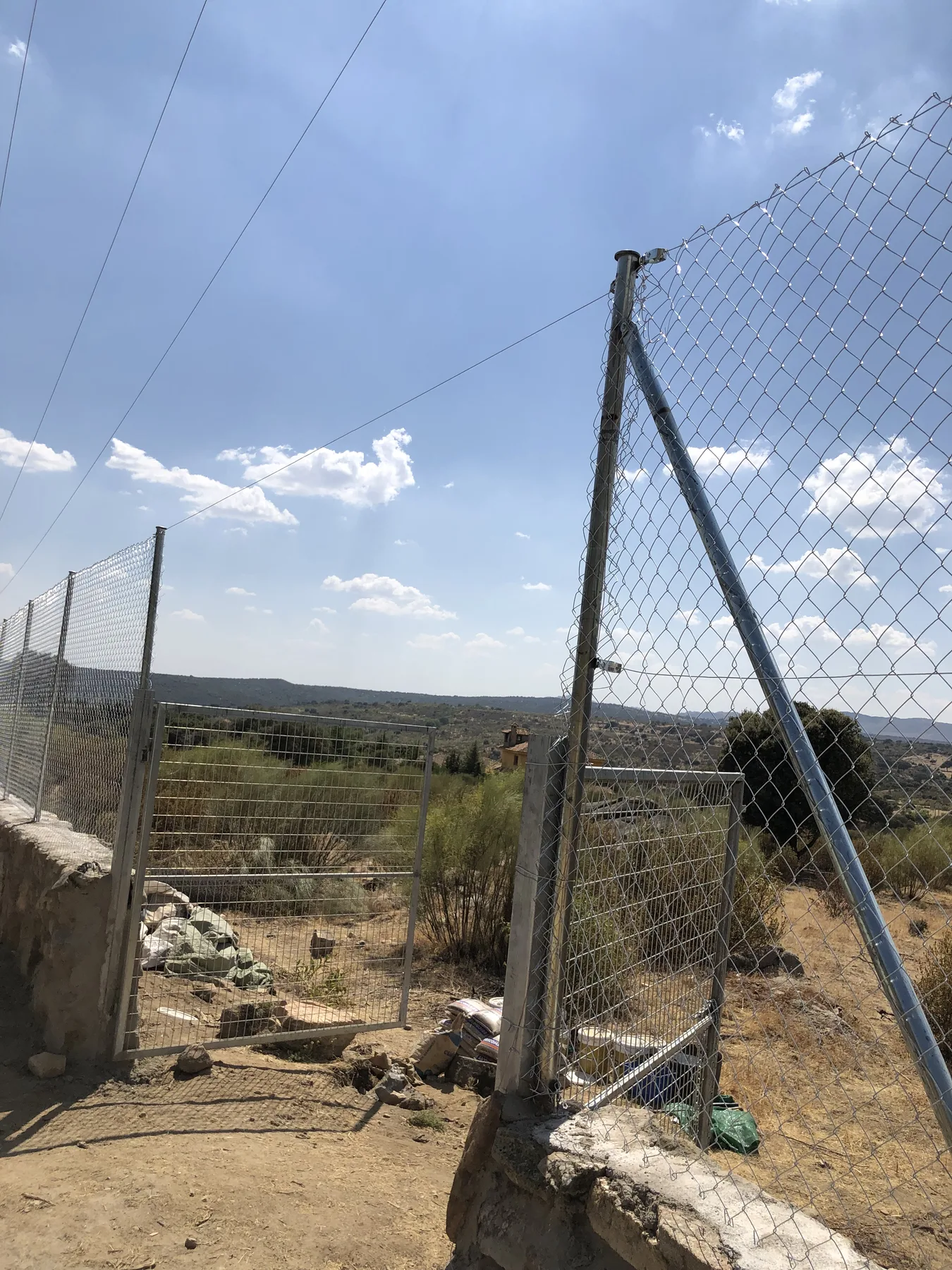 Puerta metálica y cerramiento de malla instalados sobre muro de piedra