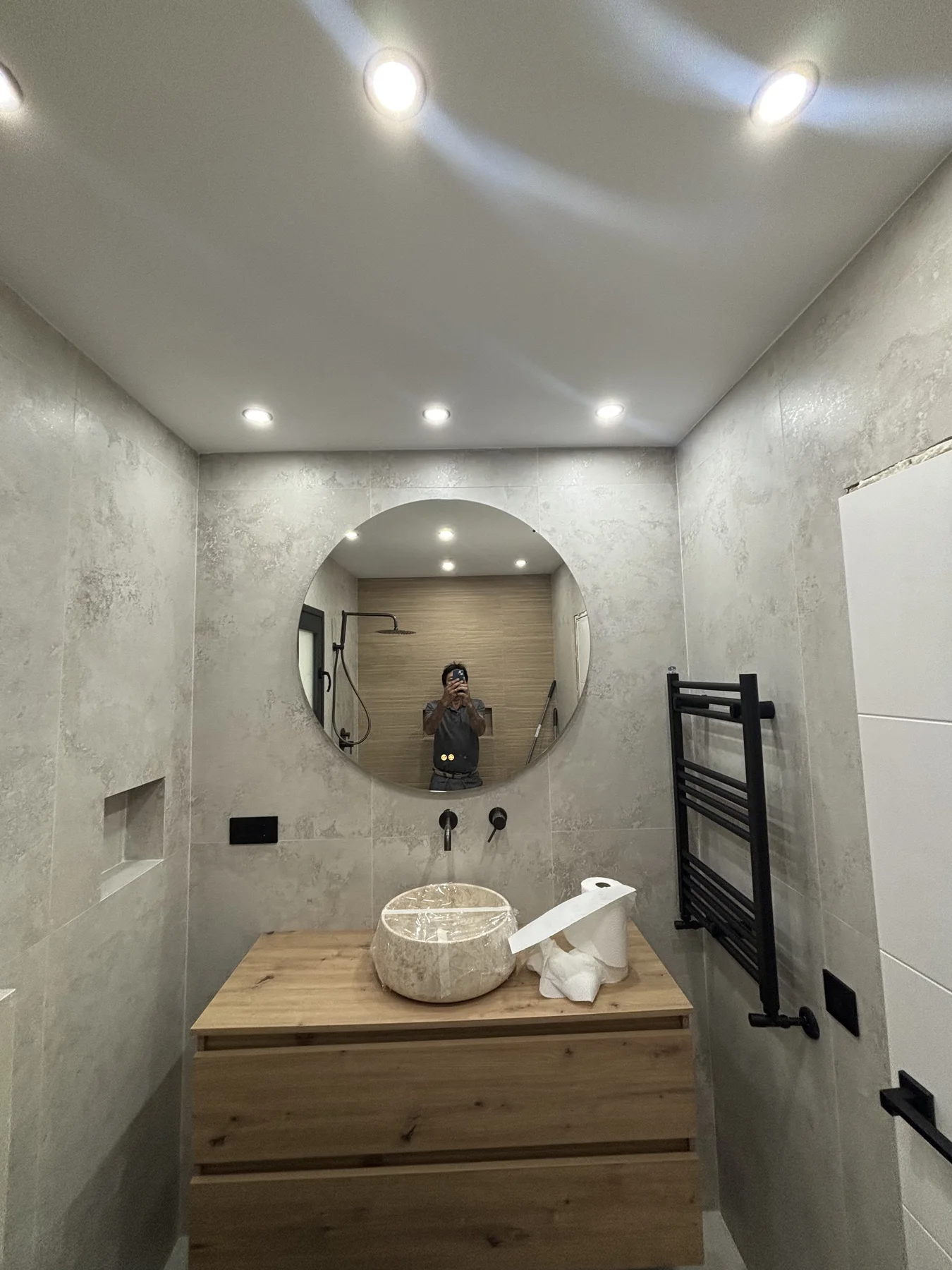 Detalle de baño reformado con espejo redondo, iluminación empotrada y acabados claros