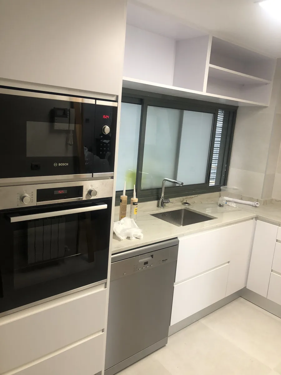 Cocina reformada con horno en columna, lavavajillas y fregadero bajo ventana