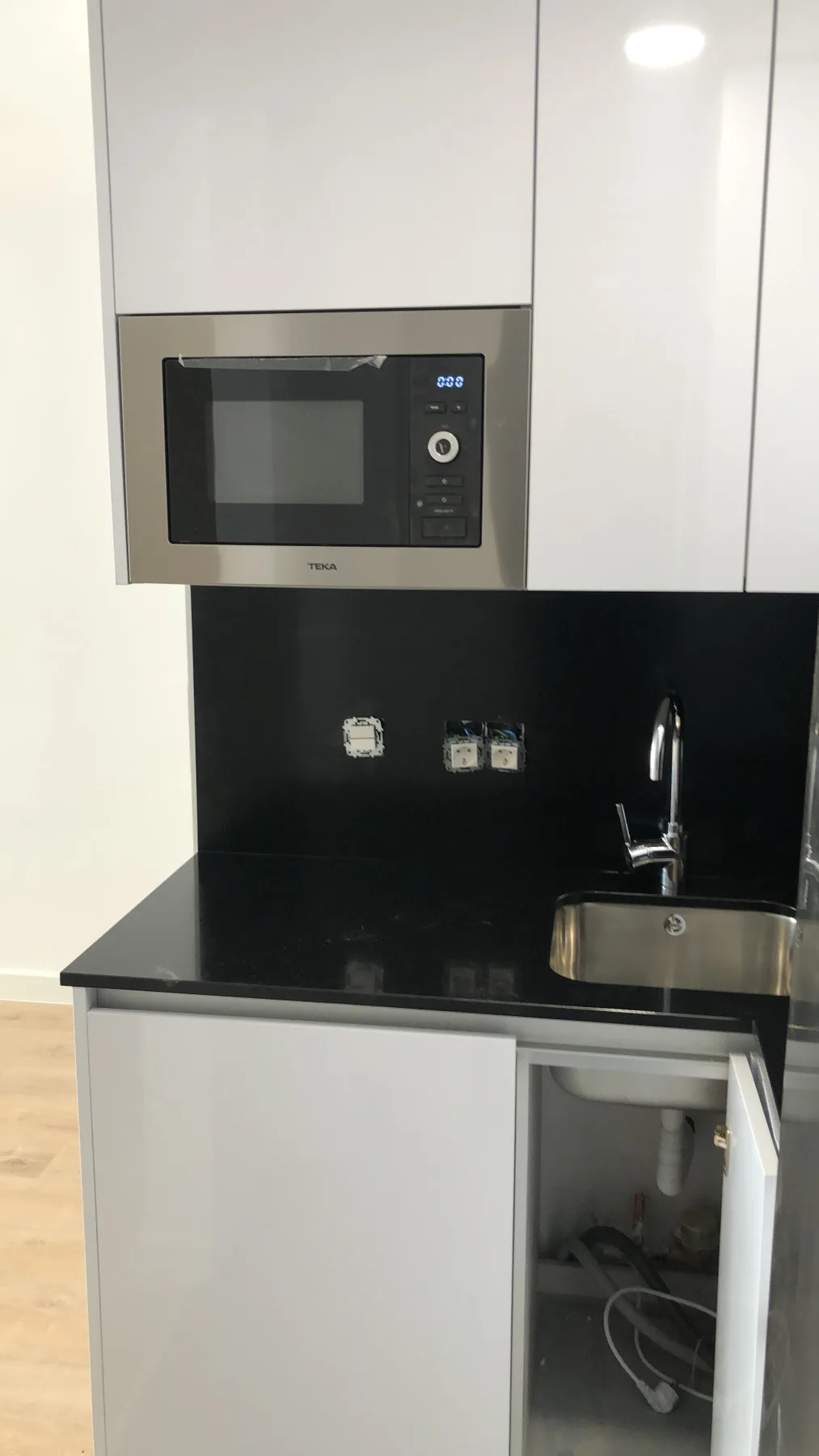 Detalle de fregadero, microondas integrado y frente negro en cocina reformada