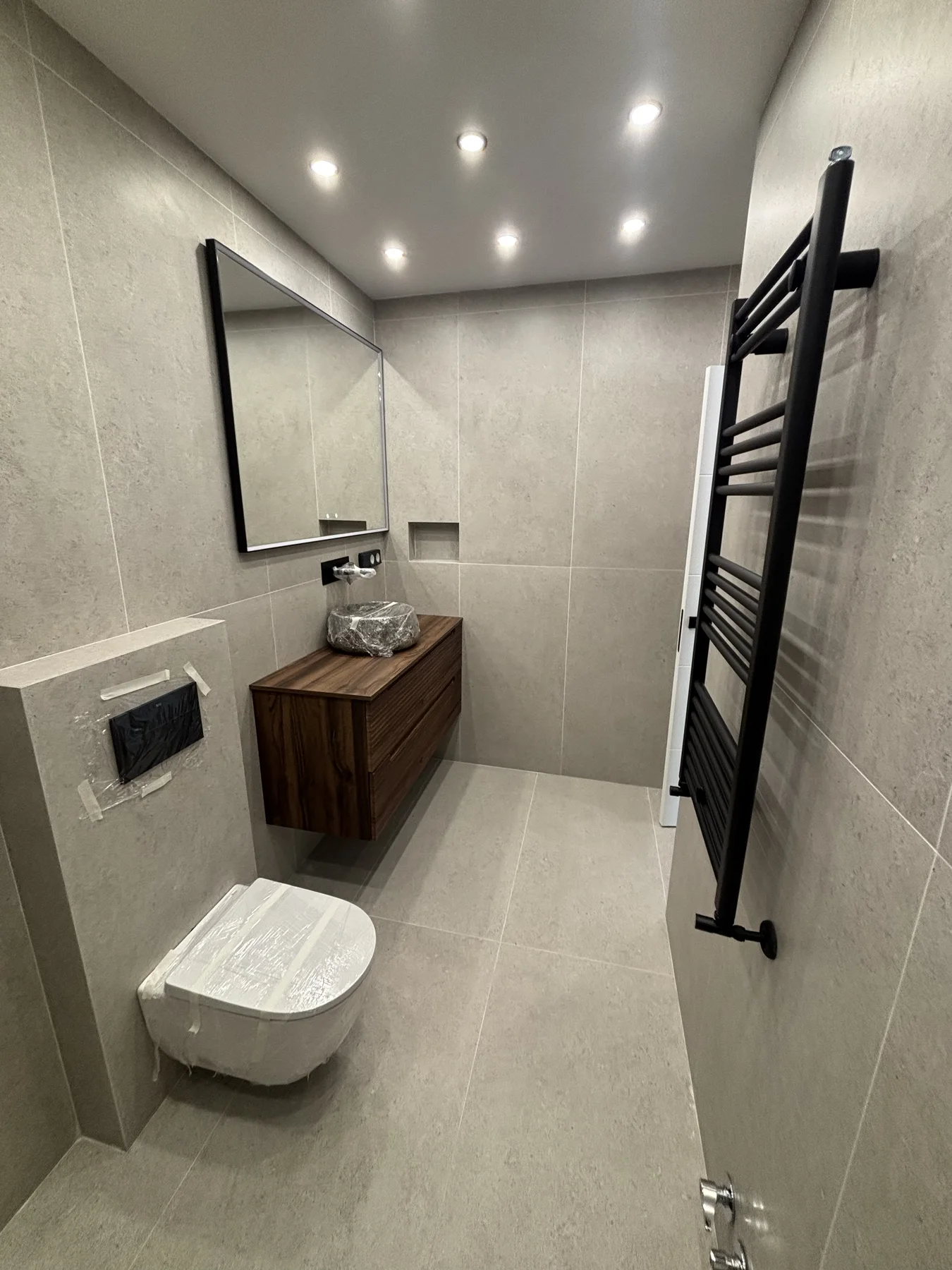 Baño contemporáneo con mueble de madera suspendido, espejo y toallero negro